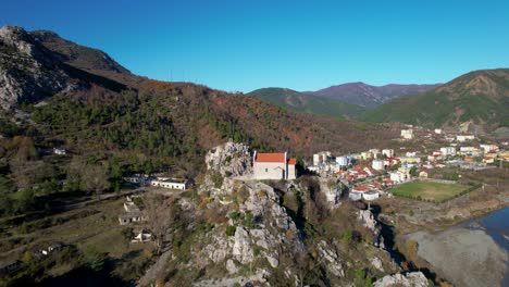 Antigua-Iglesia-Del-Monasterio-En-Rubik,-Albania,-Encaramada-Sobre-Una-Roca-Junto-A-Las-Majestuosas-Montañas-Y-El-Río