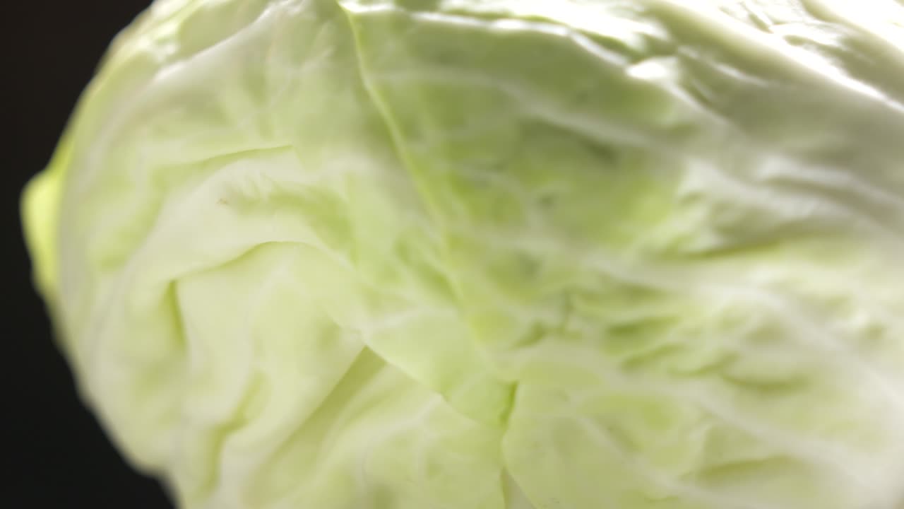 repollo blanco fresco girando sobre un fondo negro en primer plano.