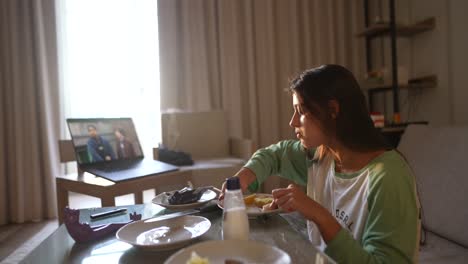 mujer joven comiendo mientras ve una película o un programa en la computadora portátil