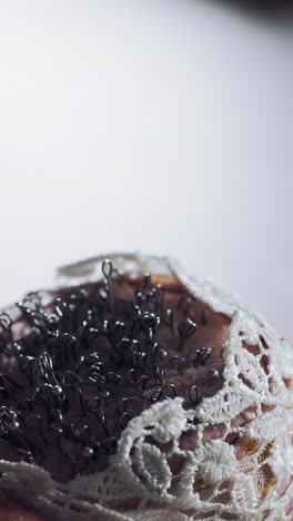 female hand with beautiful nails taking pins from the white small pincushion. a lot of sewing pins in a sponge for dressmaker on the wooden table. close-up. vertical video