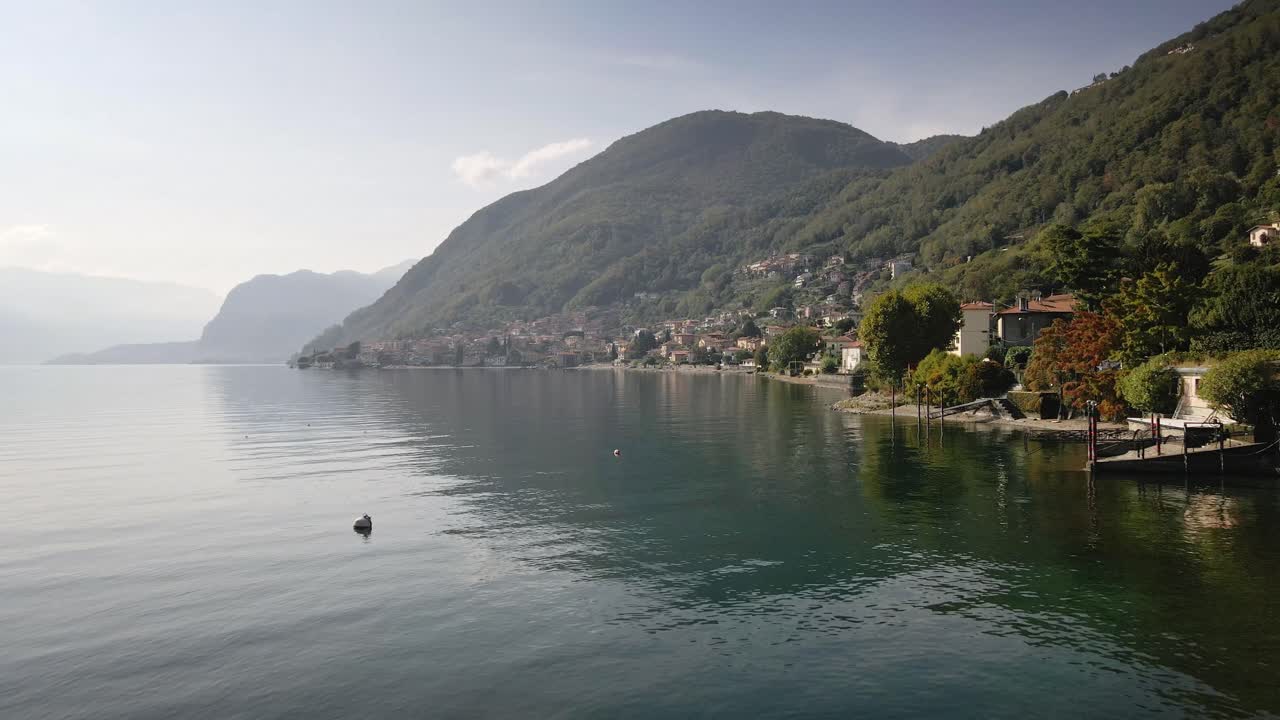 A captivating drone shot flying close to the town of Acquaseria in Lake Como, revealing its charming architecture, serene waterfront, and picturesque mountain surroundings.