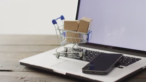 Boxes-in-shopping-trolley-and-smartphone-on-laptop-keyboard
