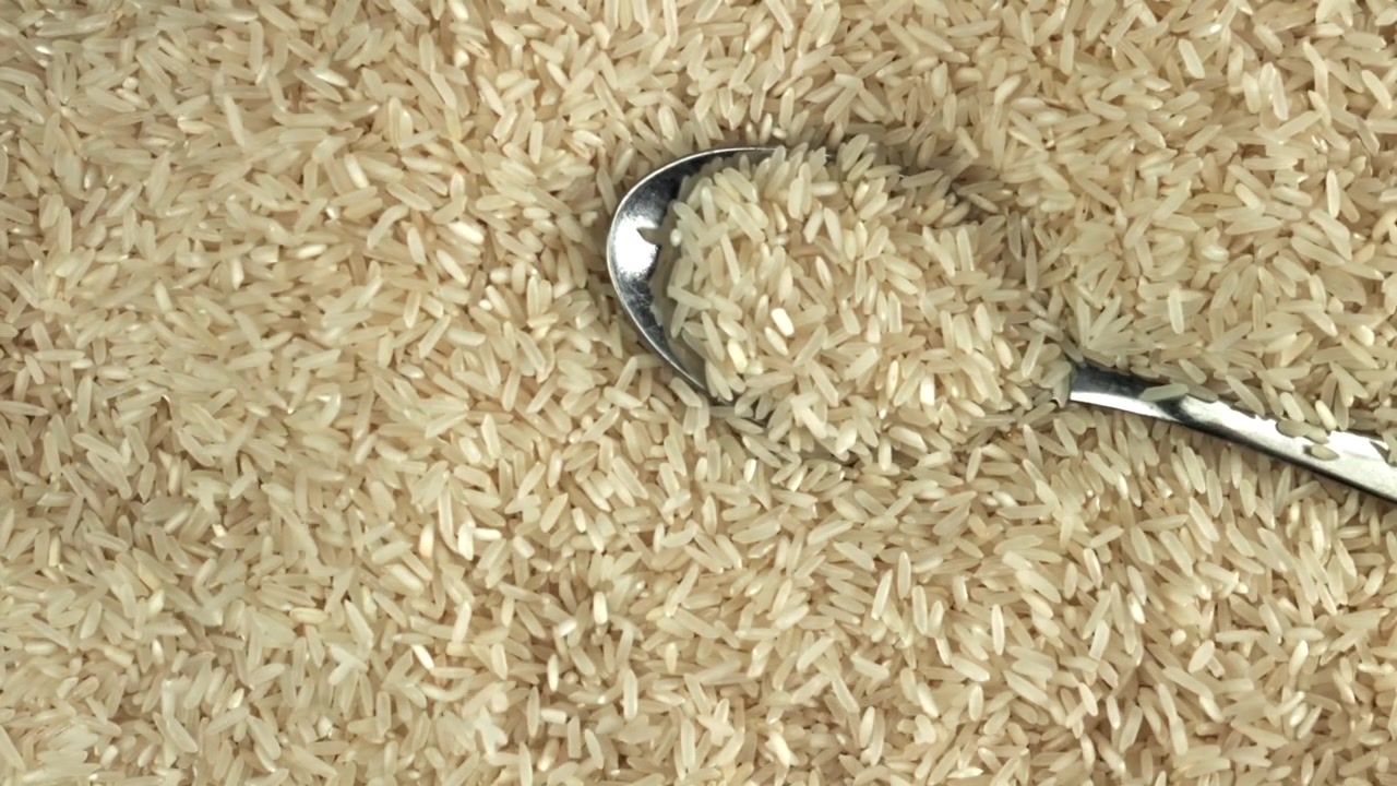 Chicchi di riso crudo che cadono da un cucchiaio su un letto di riso