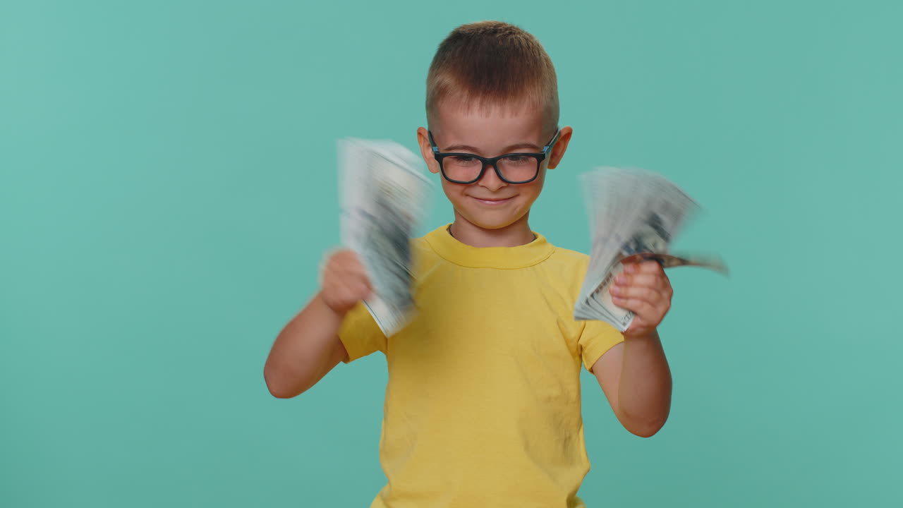 Niño pequeño sosteniendo un abanico de billetes de dólar, celebrando y bailando como ganador de lotería.