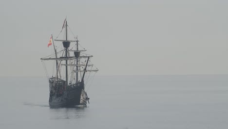 ferdinand magellan nao victoria carrack réplica del barco con bandera española navega en el mediterráneo al amanecer en un mar tranquilo frente al mar disparado en cámara lenta 60fps