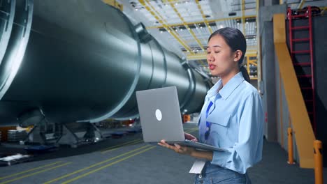 vista lateral de una mujer de negocios asiática usando una computadora portátil mirando a su alrededor en una fábrica de fabricación de tubos