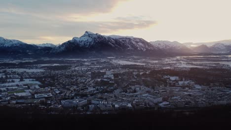 Paisaje-Urbano-De-Salzburgo-Cubierto-De-Nieve,-Castillo-Y-Alpes-Montañosos-Al-Atardecer,-Aéreo