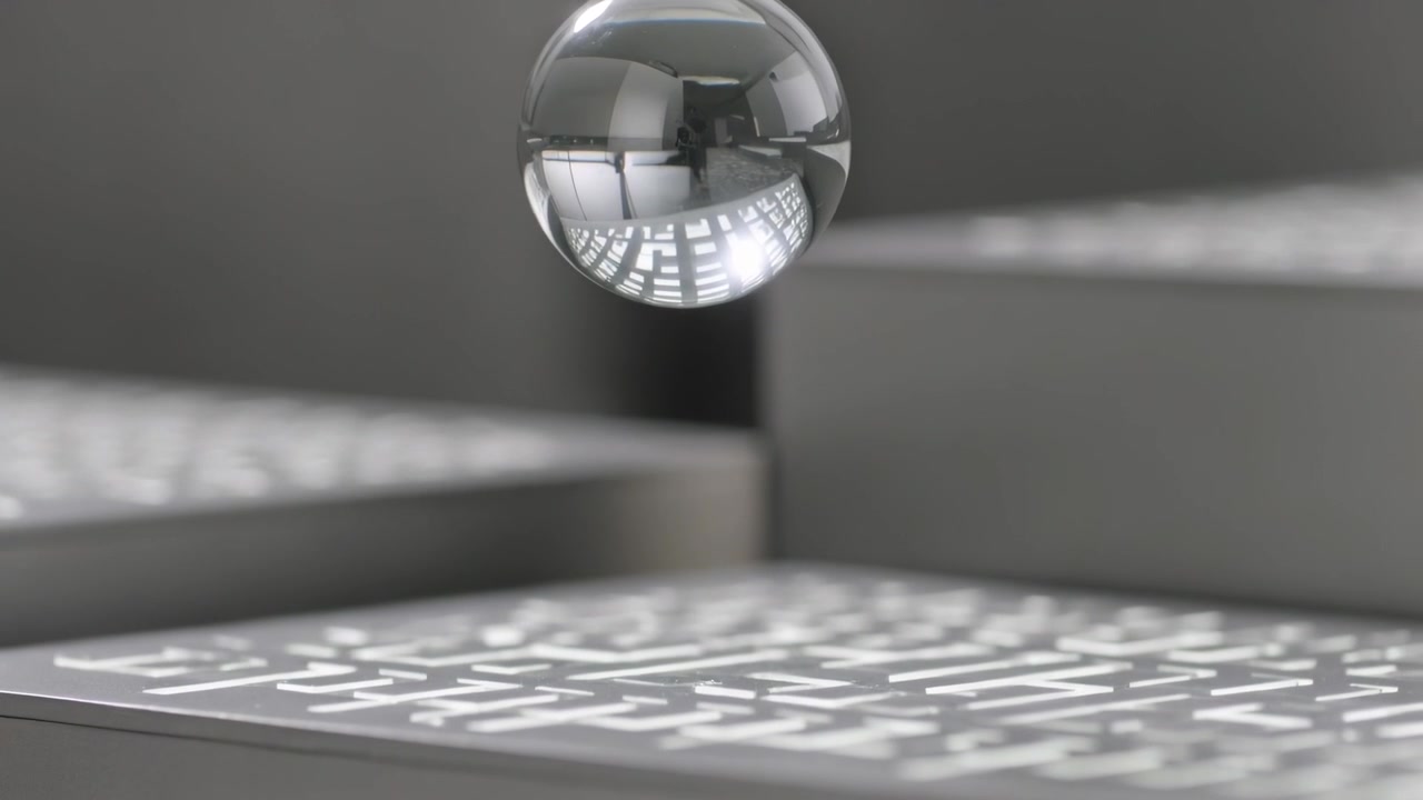 Falling clear droplet being pulled by gravity, settling above lit table panel, showing maze pattern