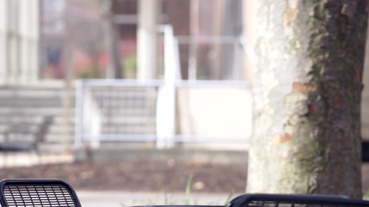 후드가 달린 재킷을 입은 한 남자가 방금 공원에 도착했고, 검은색 가방을 야외 테이블에 놓고, 공책을 들고 야외 의자에 앉아 메모를 공부했습니다.