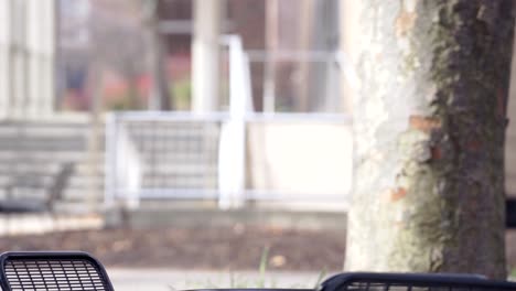 un hombre con una chaqueta con capucha acaba de llegar al parque, puso su bolso negro en la mesa al aire libre, tomó su cuaderno y se sentó en la silla al aire libre para estudiar sus notas - primer plano