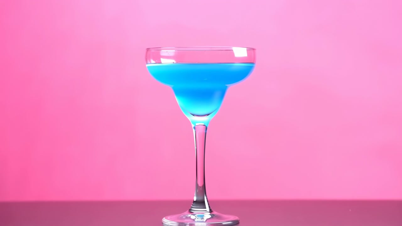 Un singolo bicchiere da cocktail con stelo riempito con liquido blu brillante è centrato su uno sfondo rosa tenue, mostrato su una superficie liscia e riflettente, pulita e uniforme
