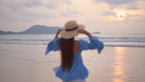 Mujer-Joven-Camina-A-Orillas-Del-Mar-Al-Atardecer-Y-Levanta-Los-Brazos