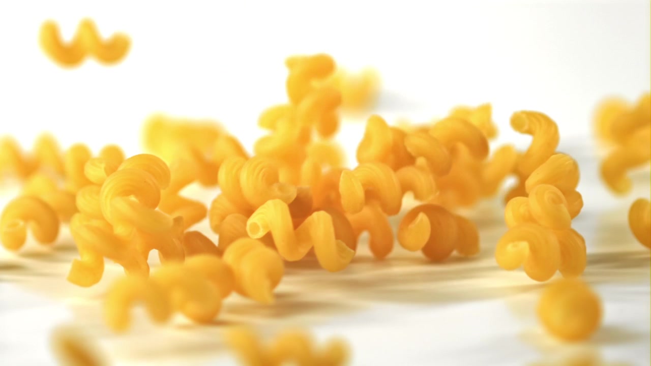 Pasta cavatappi secca che cade su una superficie bianca al rallentatore