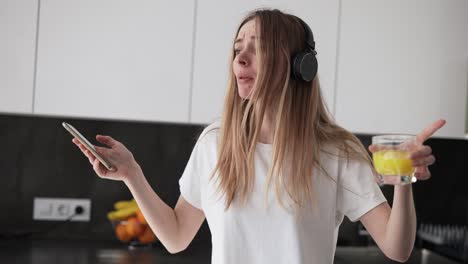 A-Young-Woman-Is-Dancing-In-The-Kitchen-And-Drinking-Juice