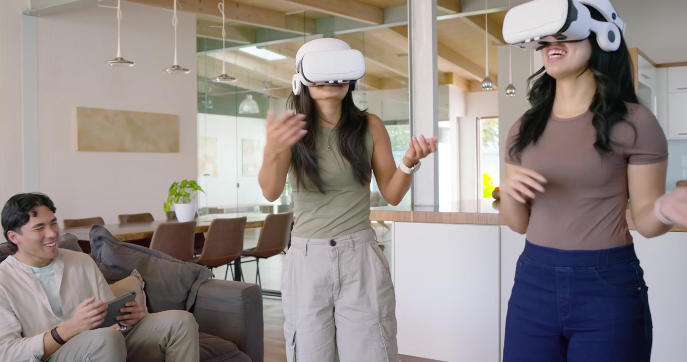 Amici di diverse etnie che indossano visori VR bianchi a casa, esplorando, mentre un uomo sul divano li guida con un tablet.