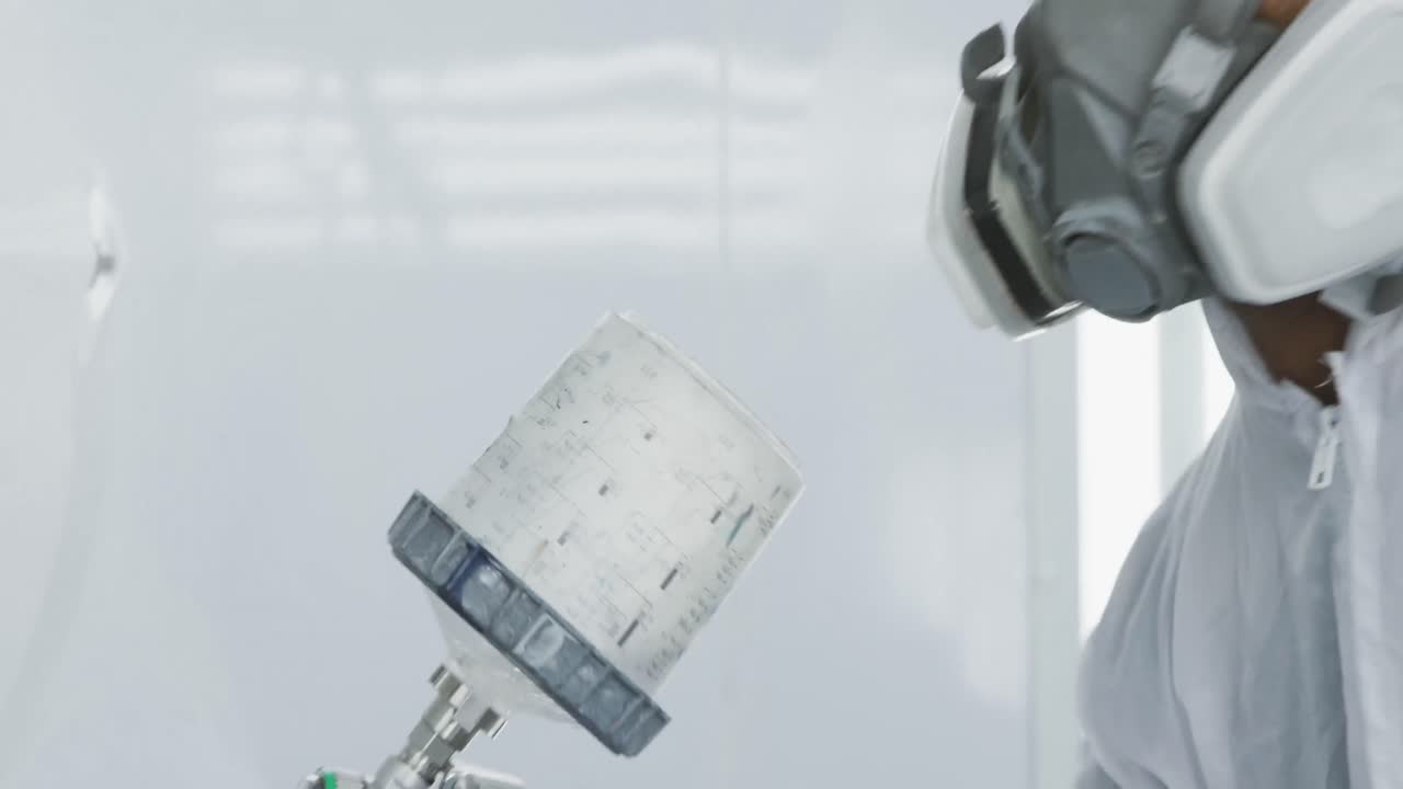 混合種族の男性自動車メカニストが 保護服を着て 車のパーツに噴射銃を使っています