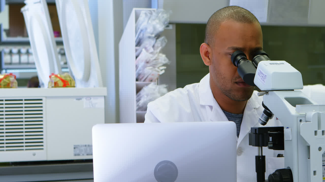 Scientist looking through microscope while using laptop 4k