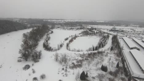 drone flying over a frozen river and frozen pond during a cold grey dark winter afternoon during snowfall