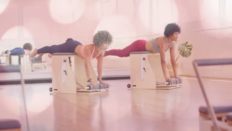 duas mulheres se exercitando em equipamentos de pilates com sobreposição de animação bokeh rosa