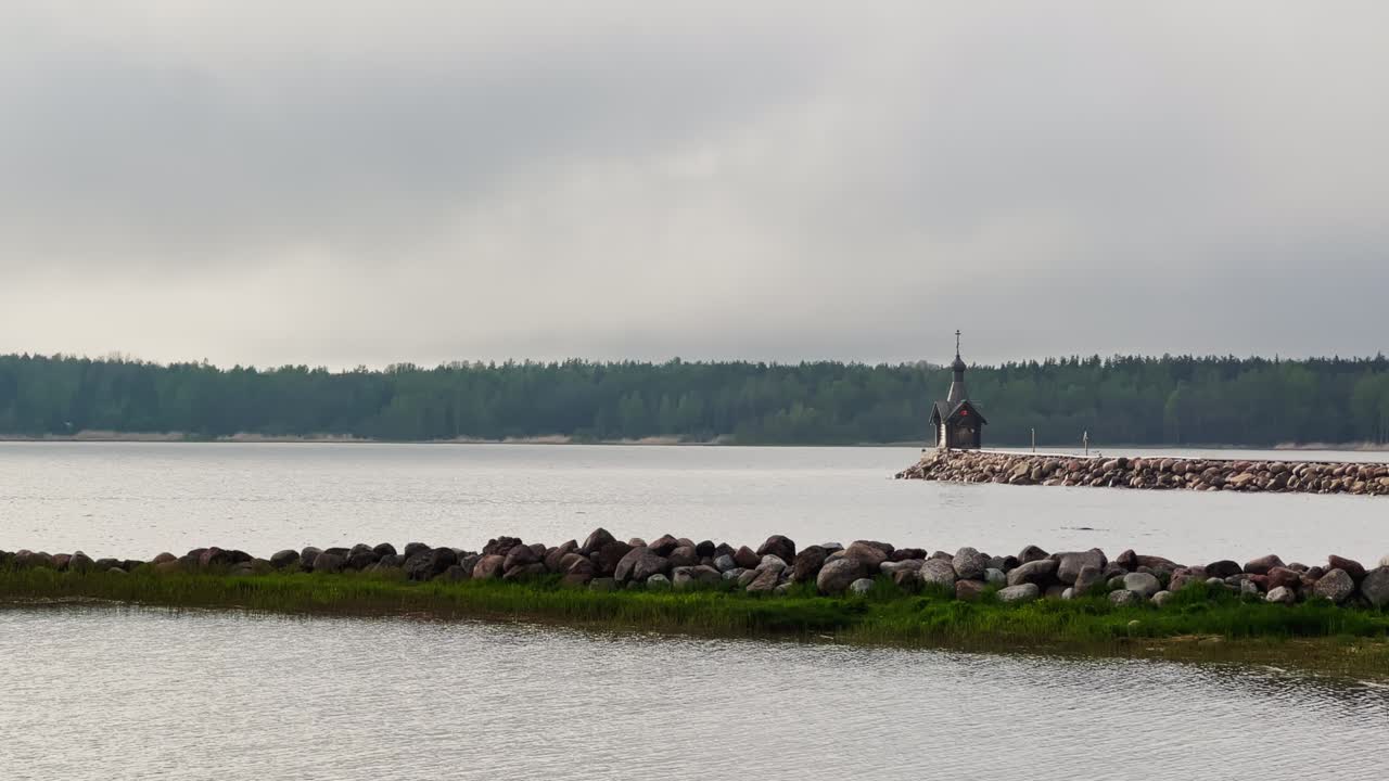 오래된 예배당은 레닌그라드 지방의 물 위에 있는 돌로 된 산꼭대기에 서 있습니다. 러시아의 구름이 많은 날씨에 숲이 배경입니다.
