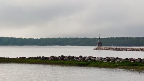 an old chapel stands on a stone promontory on the water in leningrad region russia at cloudy weather, the forest in the background