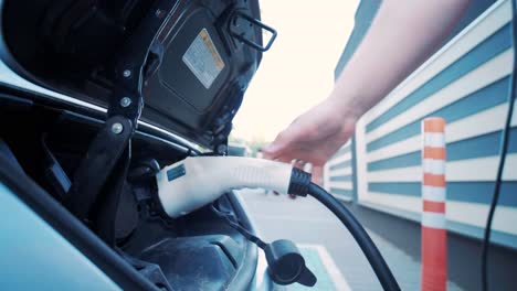 proceso de reabastecimiento de combustible de un automóvil eléctrico. un disparo debajo de la escotilla donde se carga el automóvil ecológico eléctrico. la escotella de carga del automóvil eléctrico se abre automáticamente. una mano masculina inserta un automóvil erecto