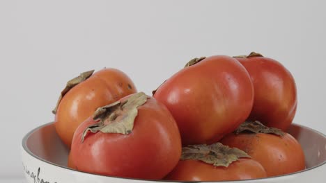 Persimmons-rotating-in-a-bowl-close-up-of-asian-persimmons-in-a-bowl-showing-stems-and-vibrant-color