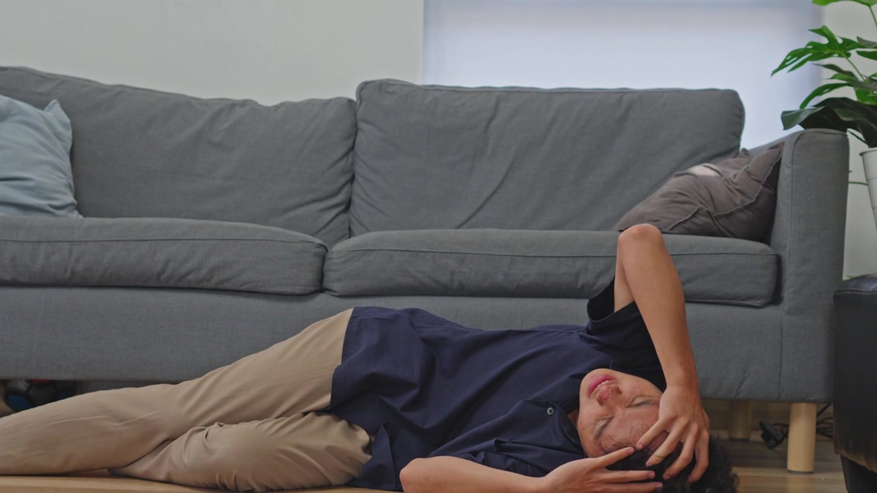 Asian man collapses holding head in intense pain during vertigo or migraine attack onto ground