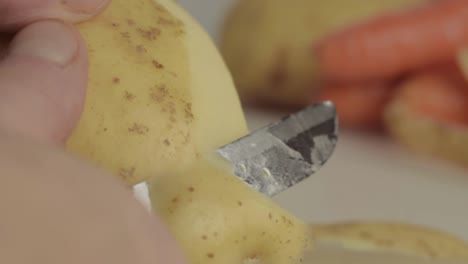 hands peeling potatoes with carrots in background macro shot