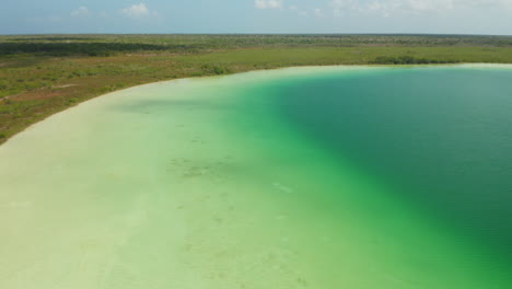 Vorwärtsflug-über-Dem-Ufer-Eines-Smaragdgrünen-Sees-Mit-Sandigem-Grund.-Wassertiefe-Beeinflusst-Die-Farbsättigung.-Kaan-Luum-Lagune,-Tulum,-Yucatan,-Mexiko