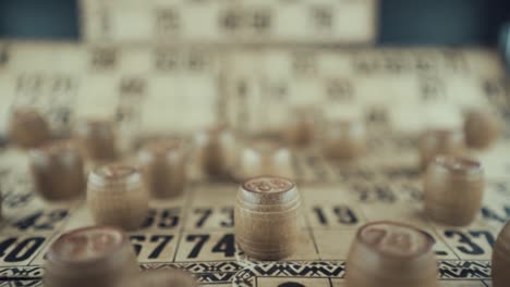 video macro de un tablero de bingo, luces de estudio, 120 fps, cámara lenta, dígitos de chips de madera, imágenes en bruto, juego de mesa de lotería, números de cartas, grúa tirando hacia atrás movimiento suave