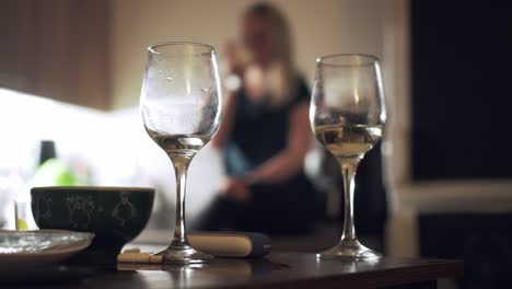 Two-glasses-of-white-wine-on-table-and-drinking-blonde-girl-in-background,-house-party-concept