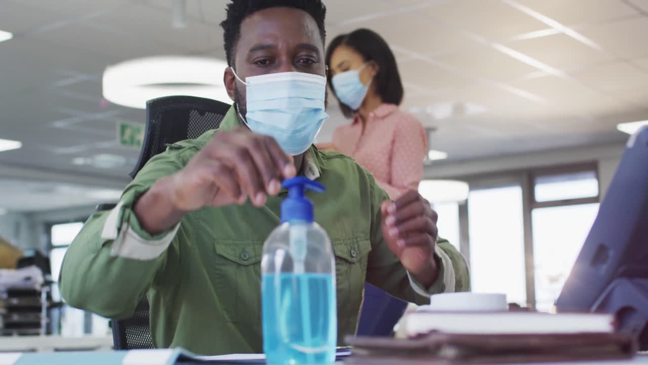 hombre con máscara facial desinfectando sus manos en la oficina