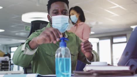 Man-wearing-face-mask-sanitizing-his-hands-at-office