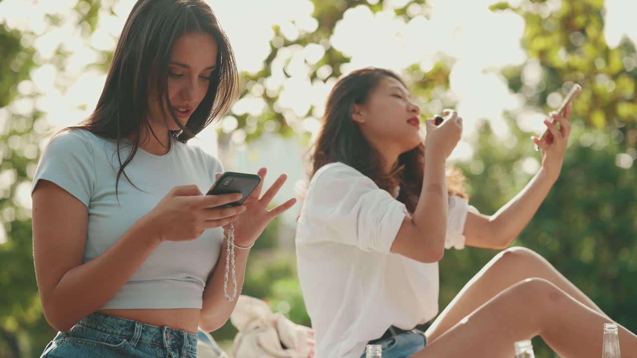Two young women enjoying snacks and mobile phones in the park