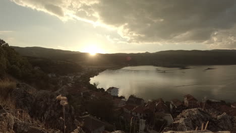 timelapse of a sunset in lin albania in the evening watching over the water with the mountains in the background on a clear day with an orange sky