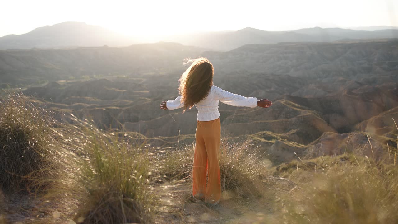 Woman with outstretched arms enjoying the vast desert landscape at sunset
