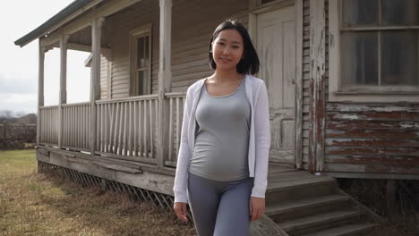 pregnant asian woman stands in front of old house