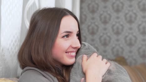 beautiful girl is sitting in her room, holding a grey cat on her hands and smiling