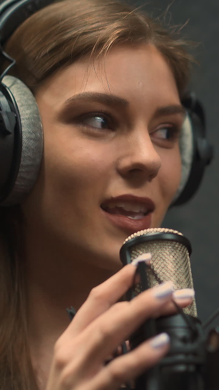 Talented blonde woman singer with black earphones records new hit with microphone in semi-dark modern soundproof audio studio extreme close view