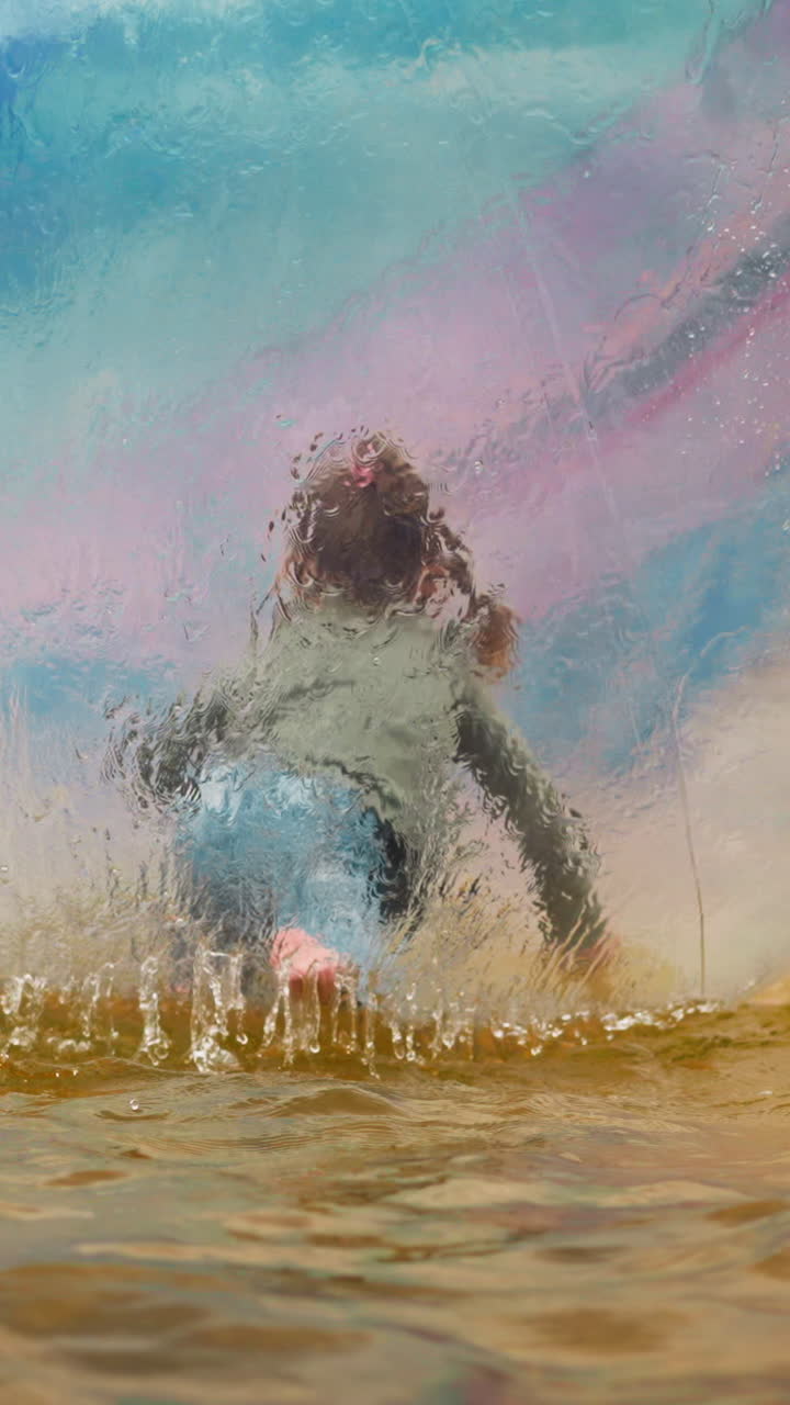 Active little girl has fun crawling inside large transparent water ball floating in small pond in city park backside view slow motion