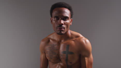 Real-Time-Studio-Portrait-Shot-Of-Tattooed-Male-Boxer-Putting-Up-Boxing-Gloves-At-Start-Of-Boxing-Match-Against-Grey-Background