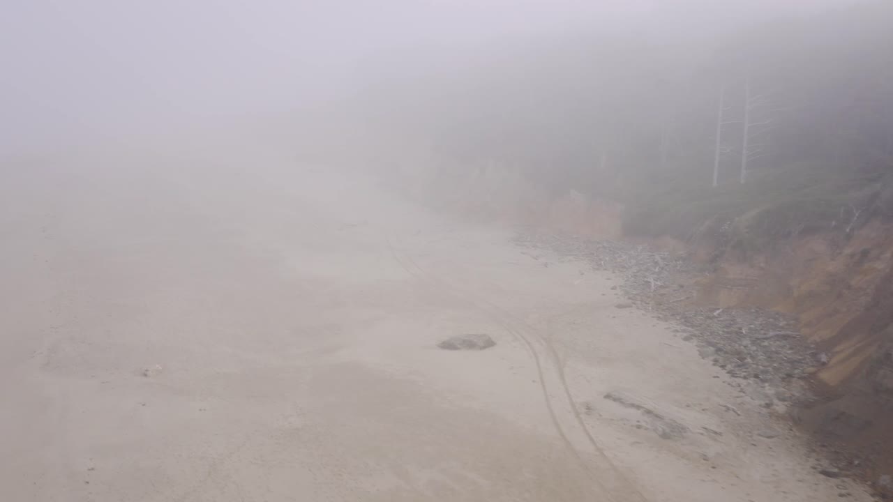 Foggy Oregon coast beach on the Pacific Northwest in a rainy day. Wet gold sand beach covered in haze. Dolly in drone flight disappears into the mist