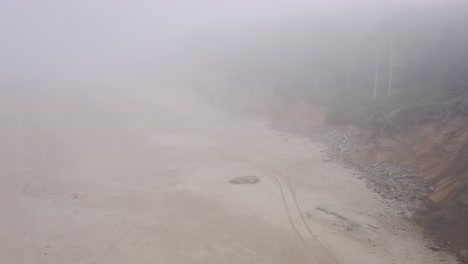 foggy oregon coast beach on the pacific northwest in a rainy day. wet gold sand beach covered in haze. dolly in drone flight disappears into the mist
