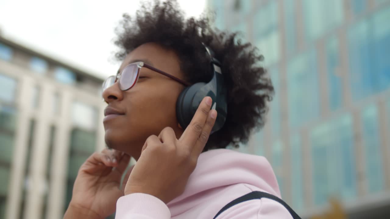 Nærbillede af glad ung afrikansk mand, der går udendørs og lytter til musik i hovedtelefoner.