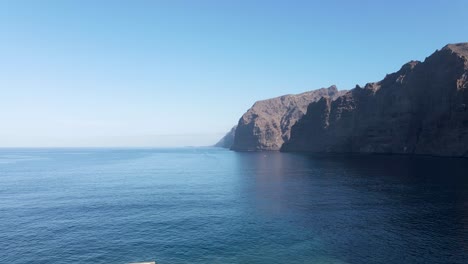 aerial drone view ascending over los gigantes harbor towards steep cliffs by the sea in tenerife, canary islands