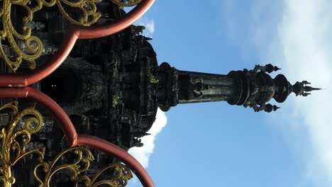 vertical tilt shot of a golden entrance gate opening to reveal the grand bajra sandhi monument, a prominent temple in bali, under the bright, sunny sky