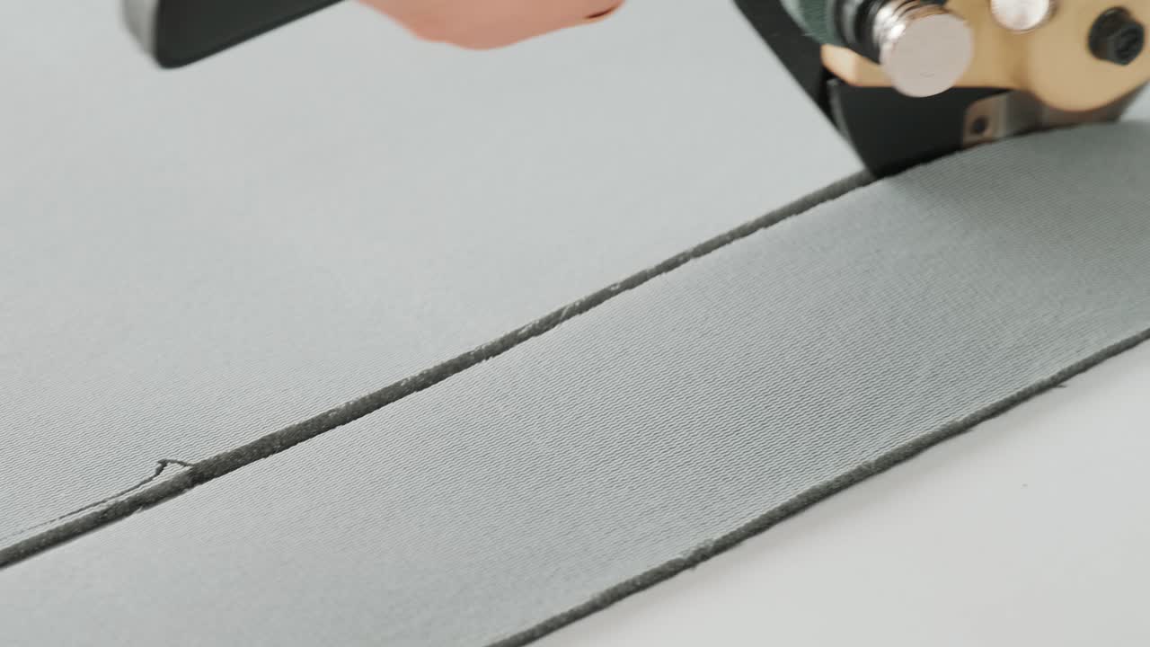 Female worker on a sewing manufacture uses electric cutting fabric machine. Sewing production line