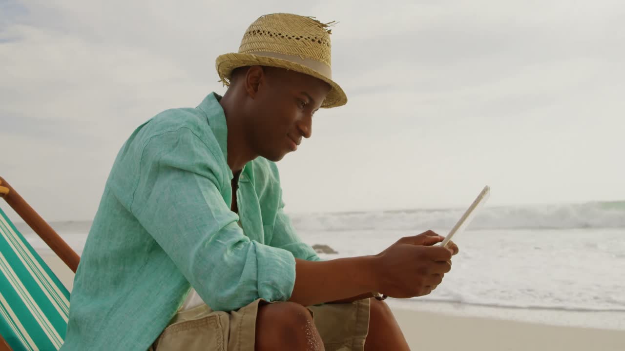 Side view of African american man using digital tablet on the beach 4k