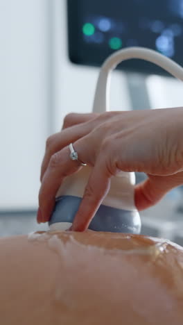 female hand sliding the ultrasonic transducer by the round pregnant belly. gel is spread by the female abdomen. close up. vertical video